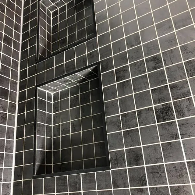 Detalj av flislagt vegg med små mørke fliser og integrerte nisjer med rene kanter.