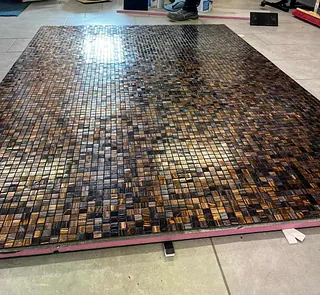 Mosaikkfliser i brune og gyldne toner lagt jevnt utover gulv under montering.
