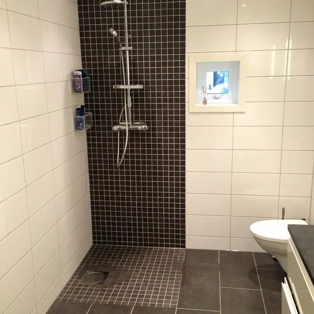 Moderne bad med dusjsone, sorte mosaikkfliser og hvite vegger med innebygget nisje.