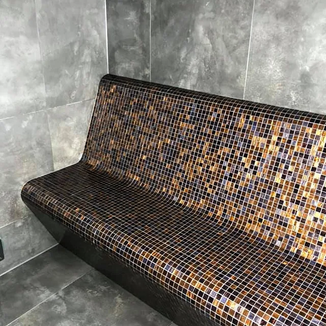 Flislagt benk med små mosaikkfliser i varme bruntoner, integrert i vegg med store grå fliser.
