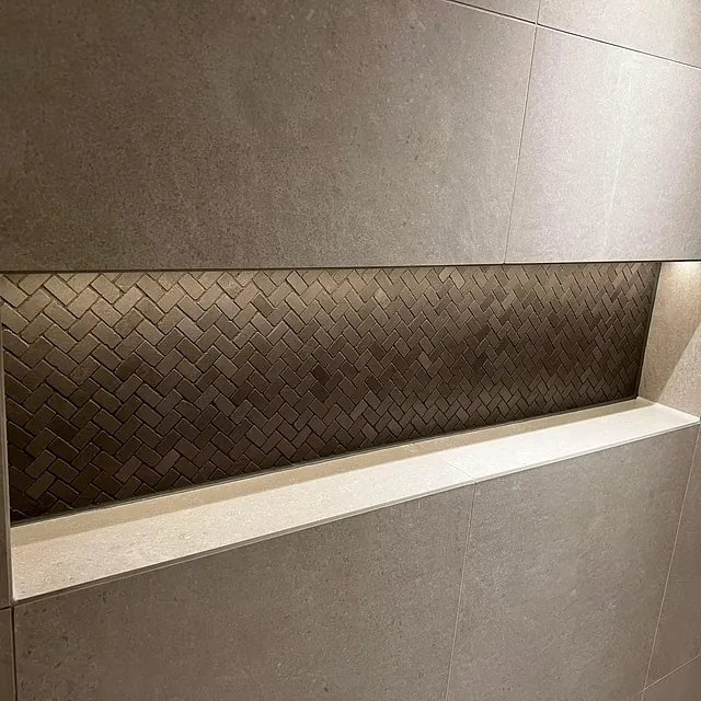 Detalj av flislagt nisje med fiskebeinsmønster og innebygd hylle i dusj med belysning.